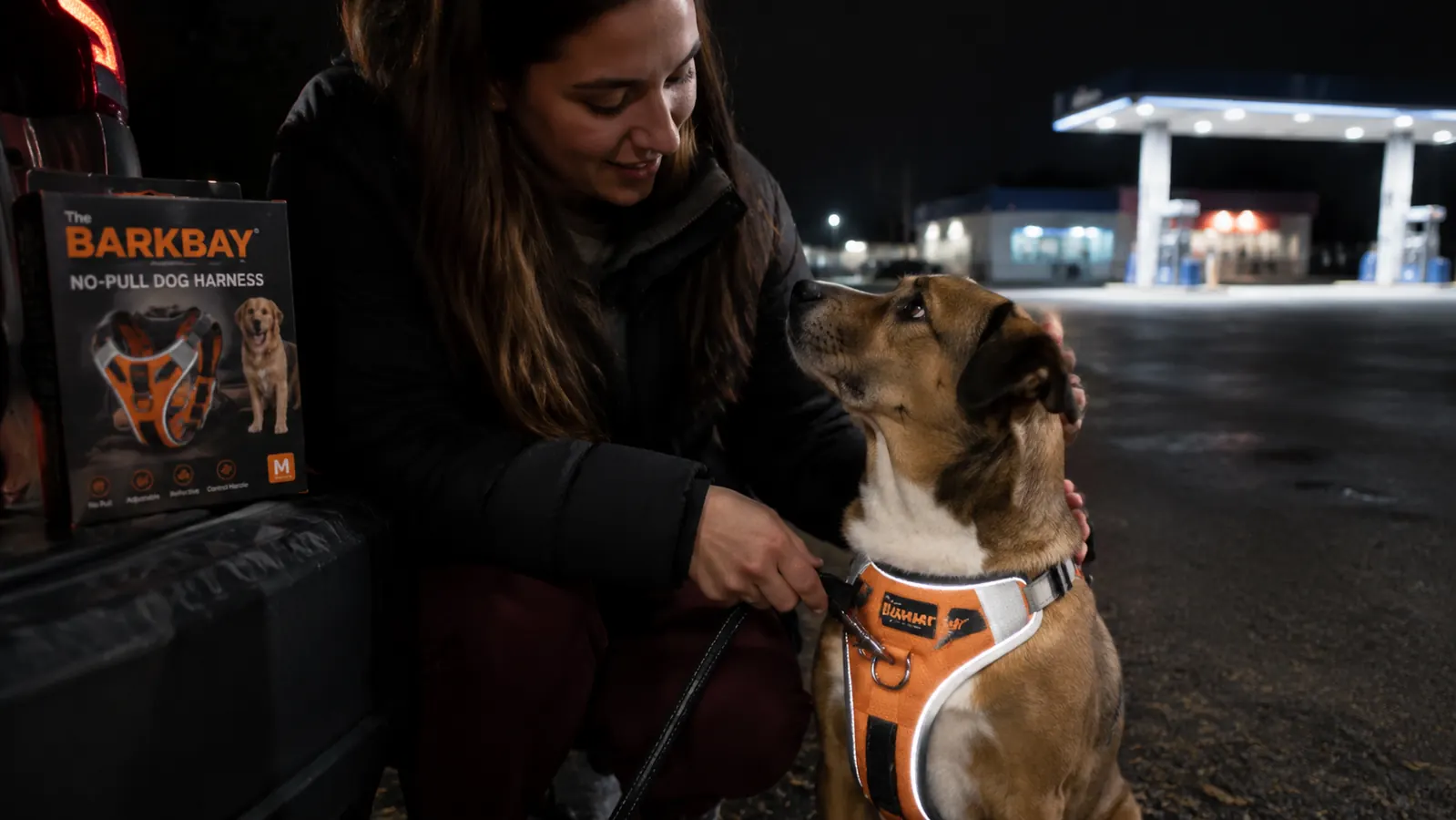 Woman clipping a leash to the front ring of a BARKBAY no-pull harness in a dim gas station parking lot